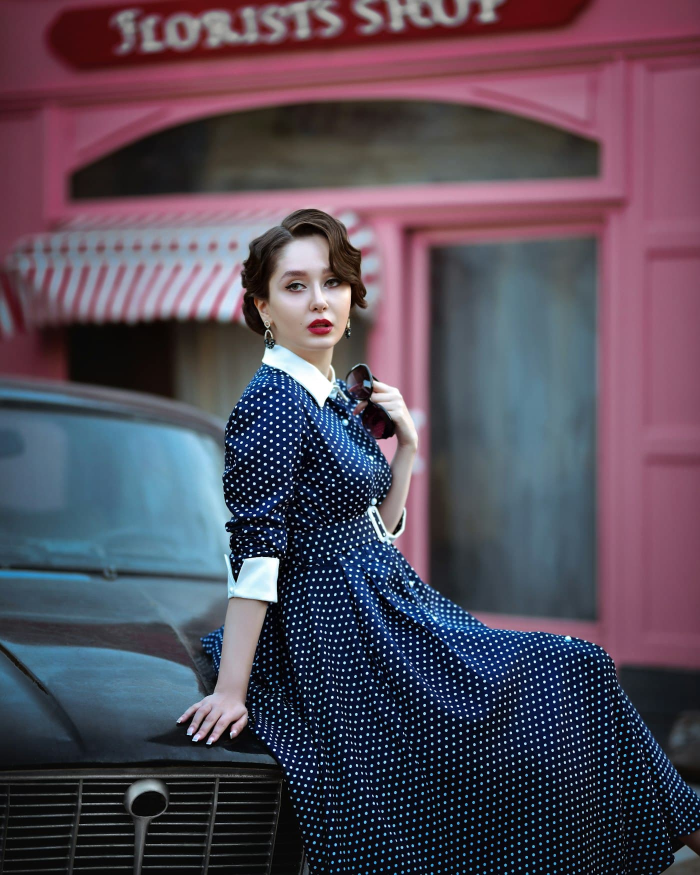 Girl in a navy polka dot vintage dress sitting on an old car